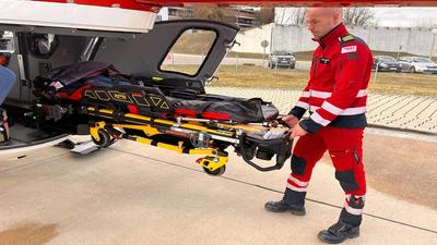 Image of electro-hydraulic stretcher-loading system being carried out of helicopter by operator