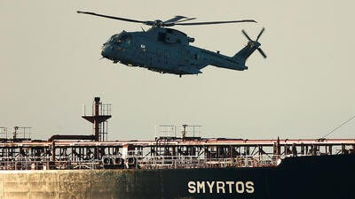 Military helicopter flying over sea next to ship