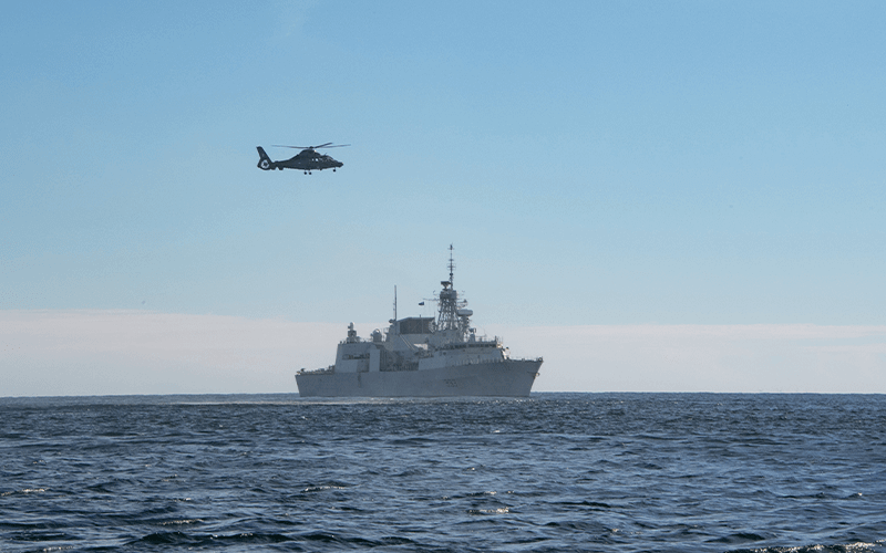 Military helicopter flying over sea with battleship in background