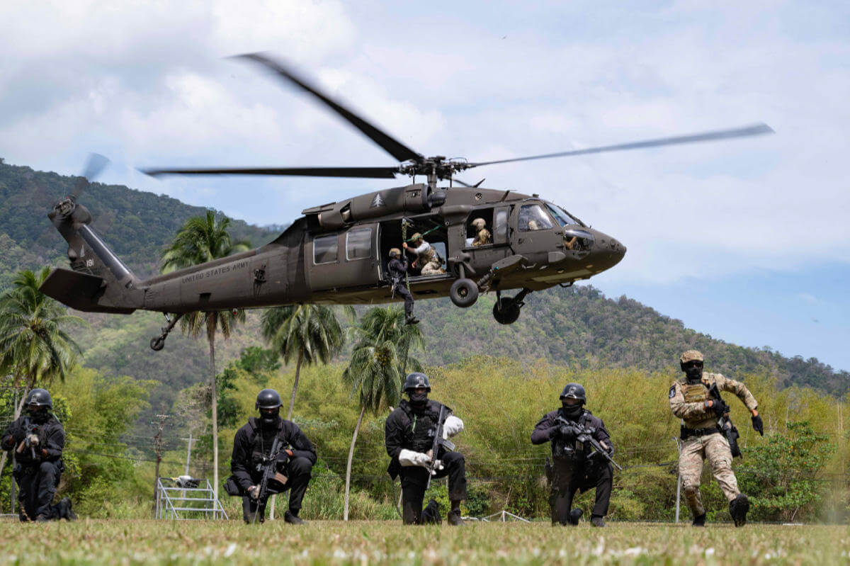 Helicopter flying with military poised below