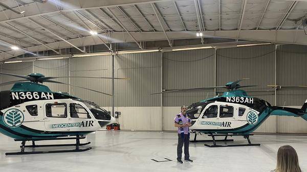 Man stands before two helicopters in aircraft hangar