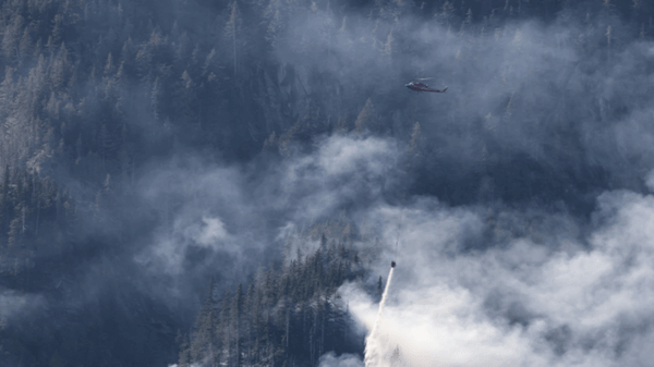 helicopter dropping fire retardant over smokey trees