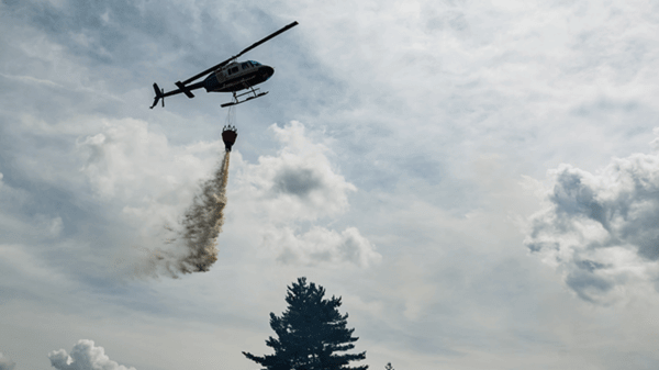 Helicopter dropping fire retardant over smokey trees