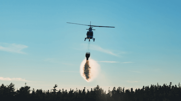 helicopter dropping fire retardant over smokey trees