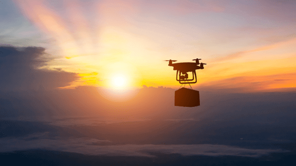 Drone carrying package in sky with sunset behind