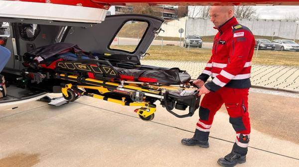 Image of electro-hydraulic stretcher-loading system being carried out of helicopter by operator