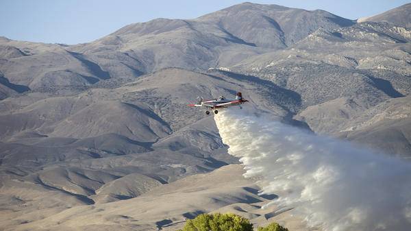 Fire rescue helicopter dropping fire retardant over trees in desert