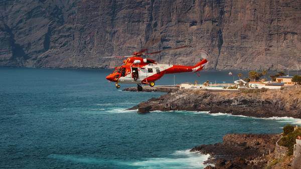 Rescue helicopter flying over rocky cliffs facing the sea