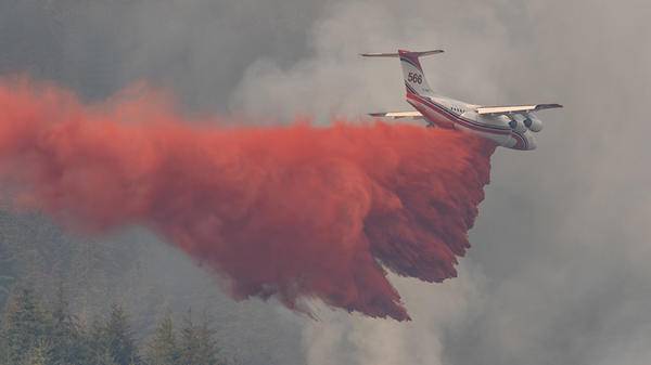 Conair plane dropping red fire retardant over forest fire
