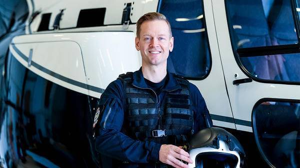 Helicopter pilot posing outside of helicopter with helmet in hands