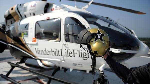Pilot holding helmet in front of helicopter 