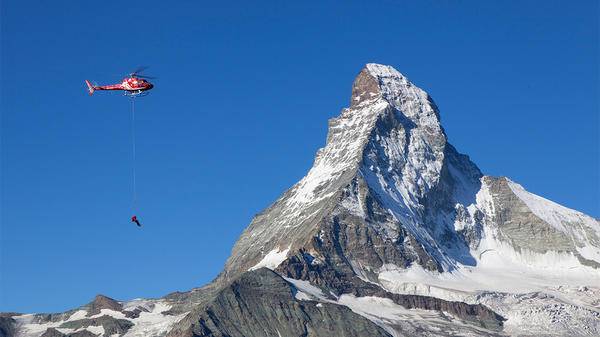 Helicopter hoisting rescue worker by mountains