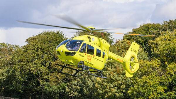 Yellow helicopter flying next to trees