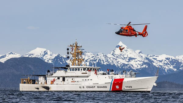 U.S. Coast Guard vessel in water with search and rescue helicopter above