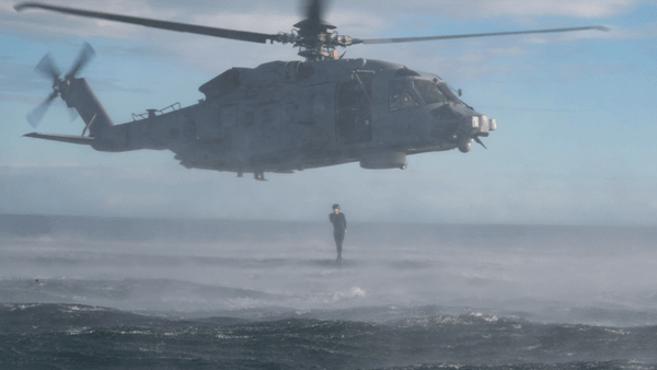 Helicopter flying over sea and diver diving out of it