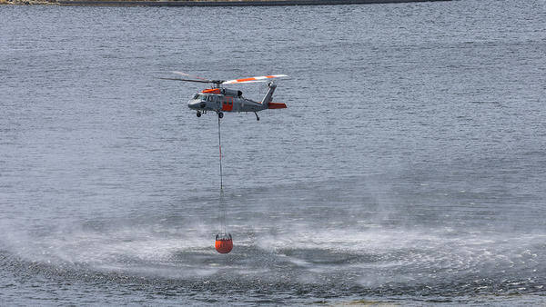 Helicopter flying above sea with fire retardant bucket