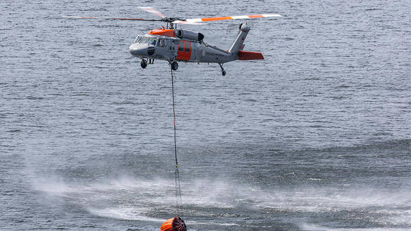 Helicopter flying above water with fire retardant nucket