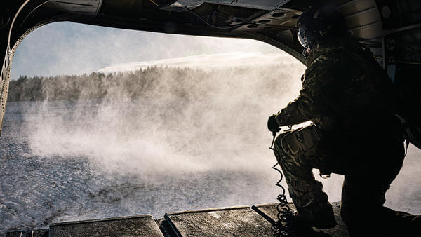 Military personnel looking out of the back of helicopter