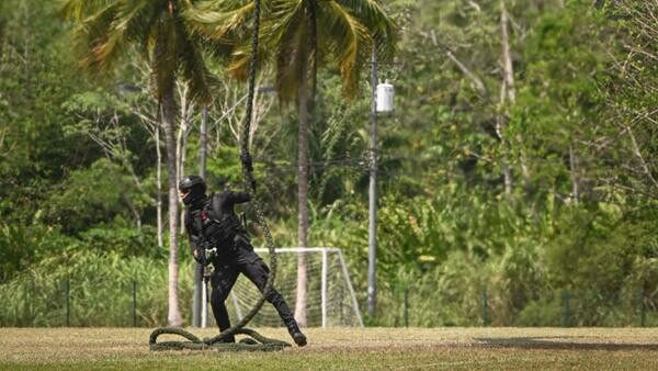 Military personnel next to rope hanging from helicopter