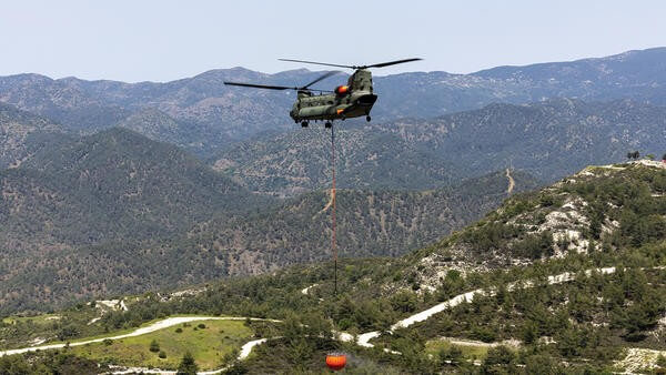 Helicopter flying above forested hills with a suspended water bucket