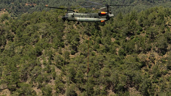 Helicopter lowering a firefighting bucket over woodland