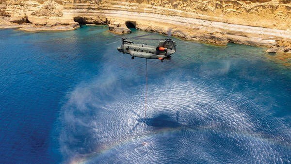 Helicopter filling a firefighting bucket from the sea.