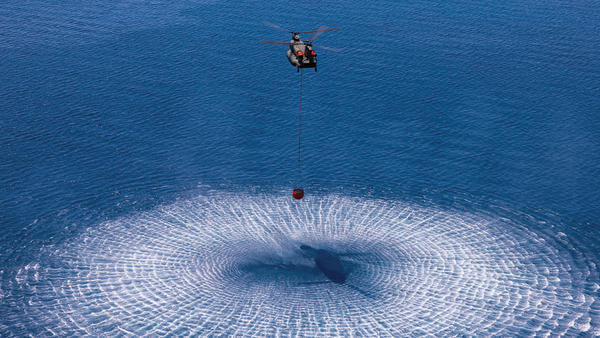 Aerial view of a helicopter collecting seawater with a firefighting bucket