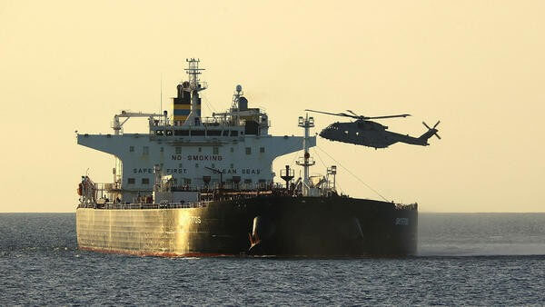 Military helicopter flying over sea next to ship
