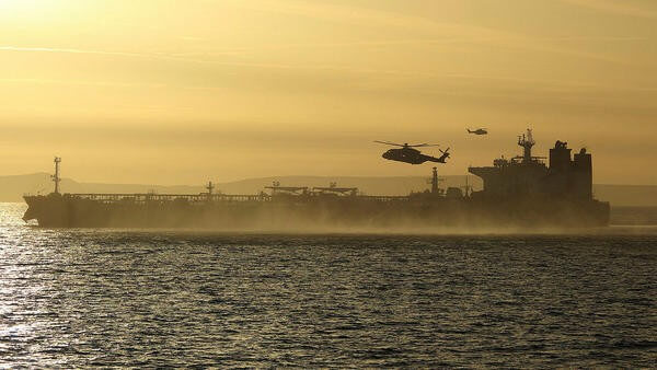 Military helicopter flying over sea next to ship