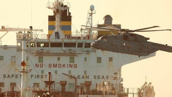 Military helicopter flying next to ship