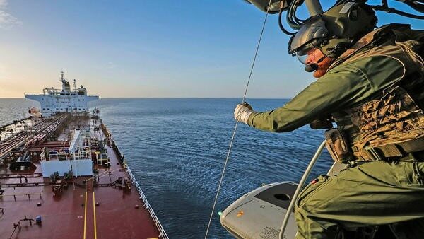 Military personel hoisting rope from helicopter above ship
