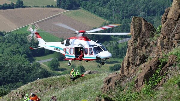 Helicopter flying by mountain with rescue workers waiting by